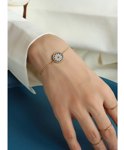Close-up of a 18K gold-plated daisy bracelet with enamel flower on a woman's wrist