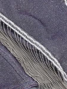 Detailed view of purple shimmering fabric with white lace edges and silver bead tassels