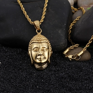 Macro shot of gold Buddha head pendant necklace with twisted rope chain on dark pebbles