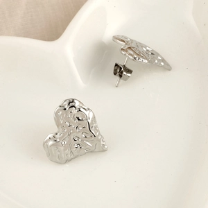 Gros plan de boucles d'oreilles cœur en argent avec texture martelée sur plateau