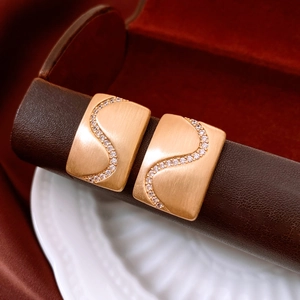 Detail of 18K gold plated rectangular earrings with wave pattern and inlaid crystals