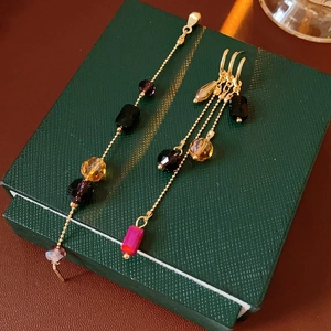 Close-up of golden tassel earrings with multi-colored glass beads on a dark green gift box