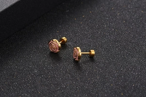 Macro detail of gold-plated rose earrings with pink enamel texture and metal backings