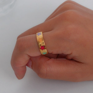 Close-up of 18K gold plated ring featuring colorful enamel star patterns on model's finger