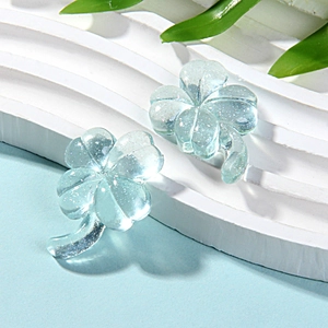 Macro shot of light blue transparent resin clover earrings with glitter on white base