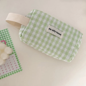 Macro detail of a green gingham quilted cosmetic bag with woven handle and fabric label