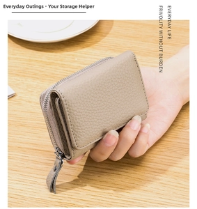 Close-up of a hand holding a beige pebble leather RFID wallet on a wooden table