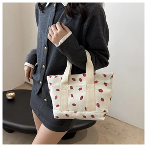 Detail of cute corduroy handbag with red strawberry prints and cream canvas straps