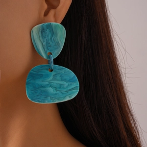 Detail of blue-green resin earrings with irregular geometric shapes worn by a model