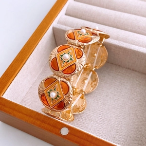 Macro shot of vintage round charm bracelet with pearl accents and orange enamel
