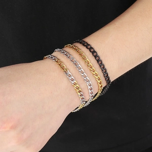 Detail view of stacked Cuban link bracelets in gold, silver, and black on a person's wrist