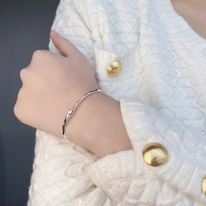 Detail of silver irregular wavy bracelet with liquid metal texture on white knit sleeve