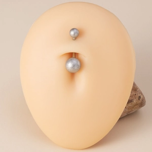 Matte stainless steel belly button ring on a silicone skin model with a stone prop
