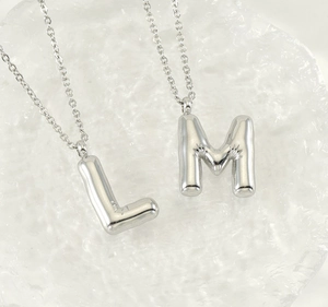 Close-up of silver balloon-style L and M letter pendants on a textured ice background