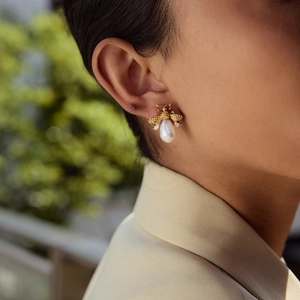 Close-up of a gold bee earring with white pearl and crystals worn by a model