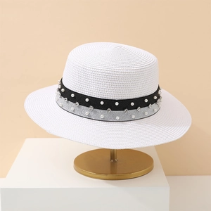 Detailed view of a white straw sun hat with pearl and rhinestone ribbon on a gold stand