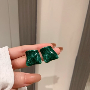 Close-up of irregular square stud earrings with dark green marble enamel and gold trim