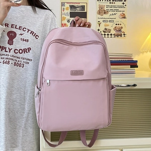 Dettaglio di uno zaino in nylon rosa con tasche laterali e logo in pelle su tavolo