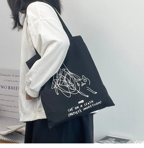 Detail of the black canvas tote bag showing artistic white cat print and task text