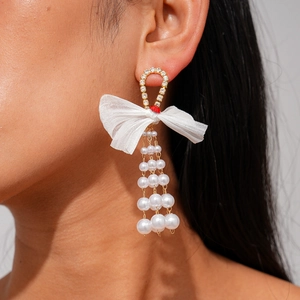 Detail of long pearl tassel earrings with white chiffon bow and rhinestone ring on model