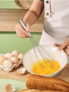 Action shot of stainless steel wire whisk blending fresh eggs in a bowl for baking
