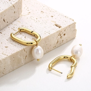 Detailed macro view of U-shaped gold hoop earrings with white pearl pendants on stone