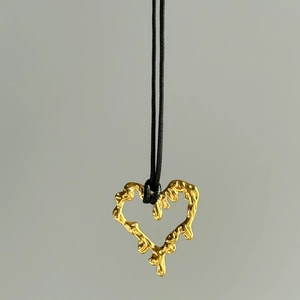 Detailed shot of golden lava heart pendant necklace with black cord on grey background