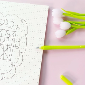 Close-up of a fluorescent green tulip gel pen on a pink background with a dot grid notebook