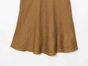 Close-up of brown textured fabric showing the natural drape and hem of the dress