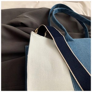 Detail of blue denim and white canvas stitching on large tote bag with blue strap