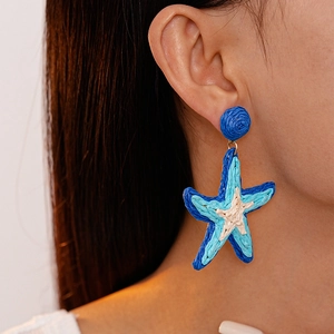 Macro di orecchini a stella marina in rafia intrecciata blu e bianca indossati
