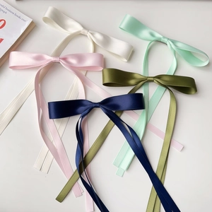 Detailed macro view of five satin bow hair clips in cream, pink, navy, and green colors