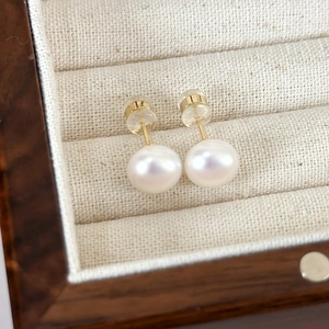 Close-up of minimalist white freshwater pearl earrings with gold pins on a jewelry box
