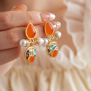 Detailed view of vintage gold earrings with orange gems and hanging pearls