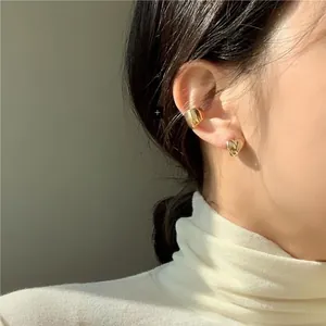 Macro view of gold-plated heart stud earring and minimalist ear cuff worn by a model