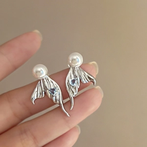 Detailed close-up of silver fish-tail earrings with white pearls and blue heart stones