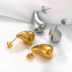 Macro detail of teardrop earrings in gold and silver finish on white silk background