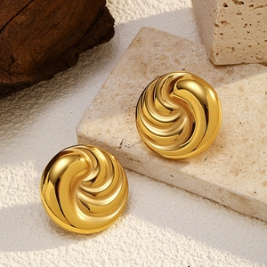 Macro shot of gold spiral textured stud earrings on stone and wood background