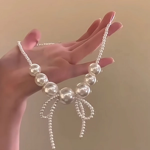 Macro detail of large pearl necklace featuring a metallic woven bow pendant and chain
