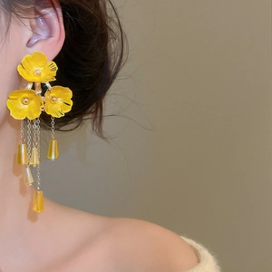Detail von gelben Blumenohrringen mit Goldketten an einem Model für ein elegantes Styling