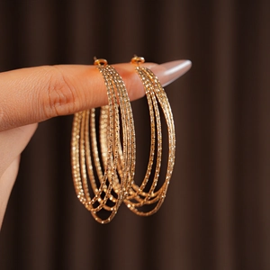 Close-up of golden multi-layer hoop earrings with textured finish held in hand
