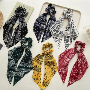 Flat lay detail showing six colors of paisley print silk scrunchies with long ribbons
