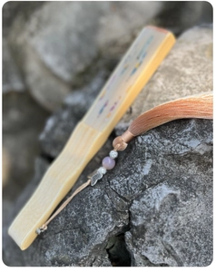 Close-up of a closed silk embroidery fan on a rock with an orange-pink tassel