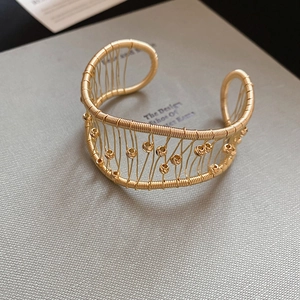 Close-up of golden woven mesh open cuff bracelet with metallic beads on a book