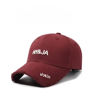 Close-up of wine red baseball cap featuring white NY&JA embroidery and frayed brim details