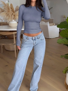 Slim fit grey long sleeve top paired with light blue jeans in a casual indoor setting