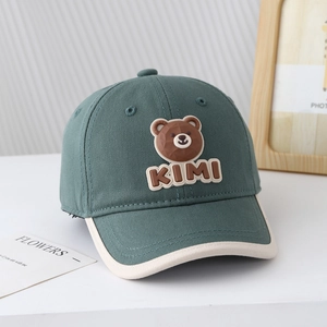 Détail de la casquette bébé avec ours 3D et broderie KIMI sur une surface blanche