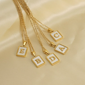 Gold shell letter pendant necklaces A to E on elegant beige silk fabric background