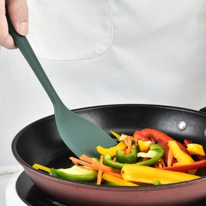Dark green heat resistant silicone spatula flipping colorful peppers in non-stick pan