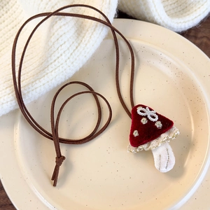 Detailed close-up of a handmade red mushroom fabric necklace on a cream knit background